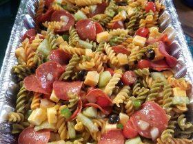 Italian pasta salad with rotini, tomatoes, mozzarella, salami, olives, pepperoncini, and herbs
