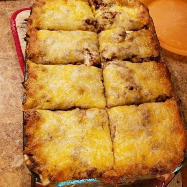 Easy ground beef burrito casserole with seasoned beef, tortillas, beans, corn, enchilada sauce, and melted cheese