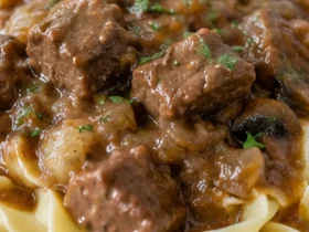 Beef tips with mushroom gravy spooned over wide egg noodles on a white plate