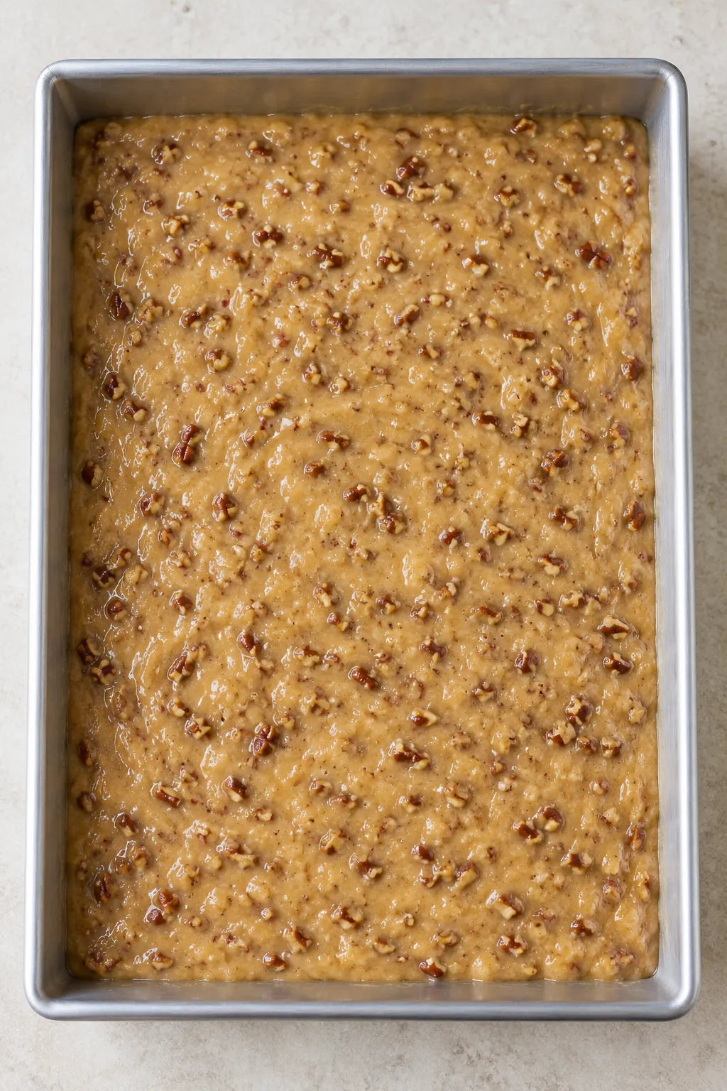 Unbaked pecan bread batter spread evenly in a greased rectangular metal pan