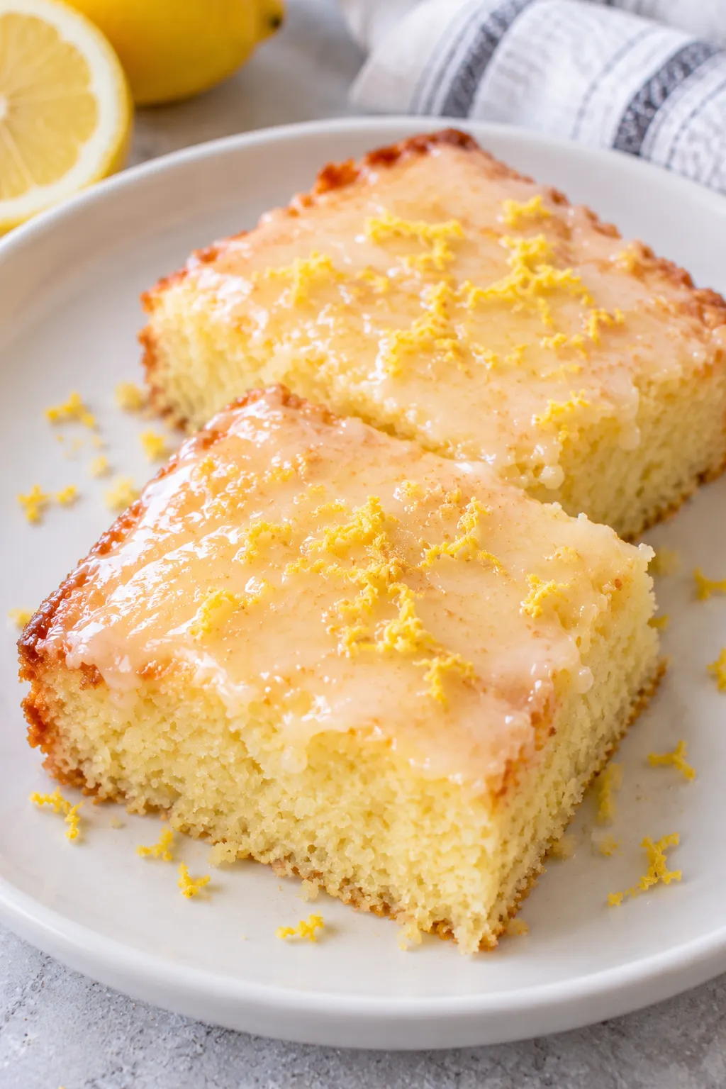 Two pieces of Lemon Cake To Die For topped with lemon glaze and zest