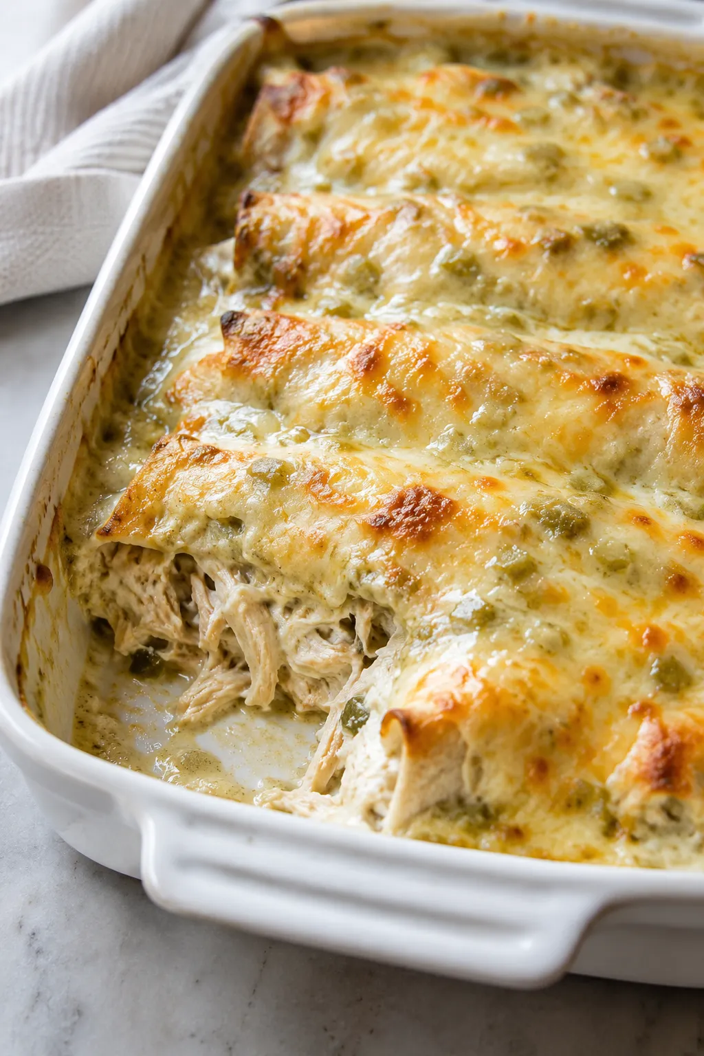 Baked cream cheese chicken enchiladas in a white casserole dish with shredded chicken filling exposed