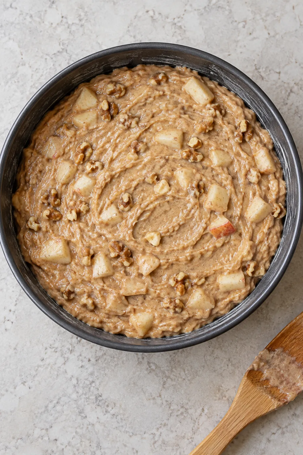 Unbaked apple walnut cake batter spread in a round cake pan