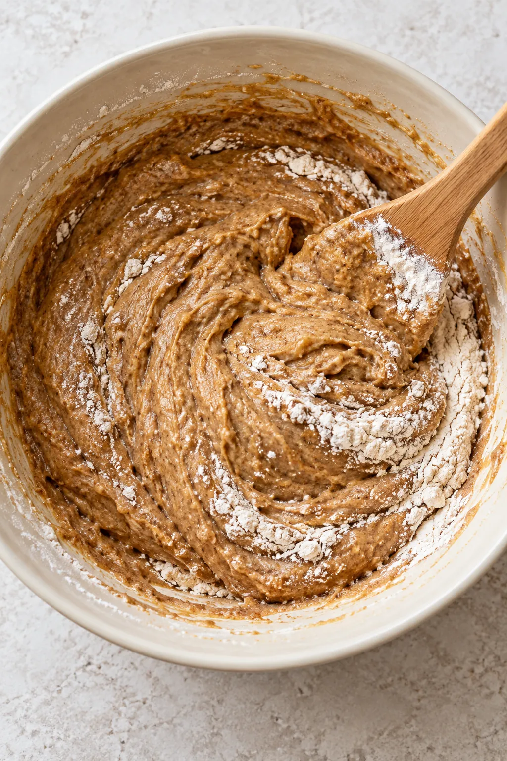 Flour being folded into cinnamon cake batter with a few dry streaks still visible