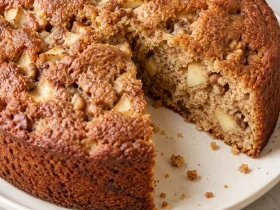 Round cinnamon apple walnut cake with a slice cut out, showing the apple-studded crumb