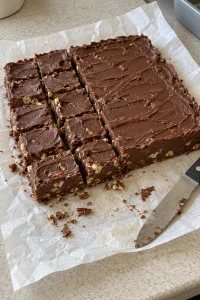 Firm chocolate pecan fudge partly cut into squares on parchment with a knife alongside