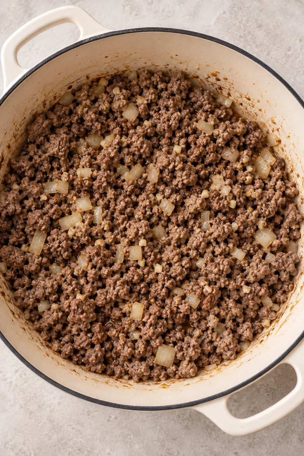 Browned ground beef and softened diced onion in a cream Dutch oven