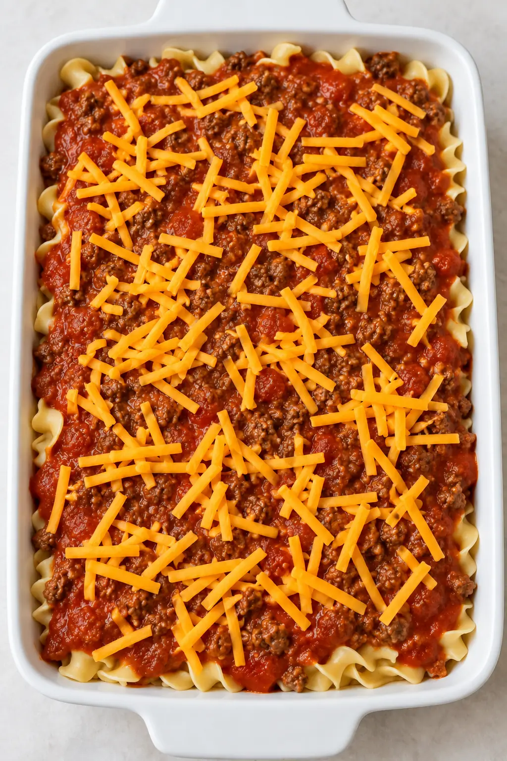 Unbaked layered casserole topped with tomato beef sauce and shredded Cheddar
