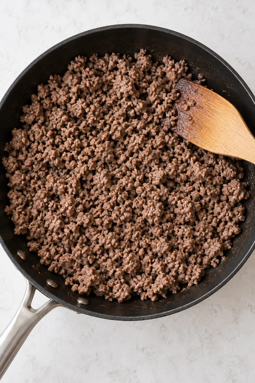 Browned ground beef crumbles in a skillet before adding tomato sauce