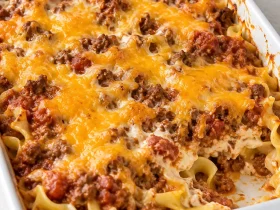 Ground Beef Casserole with egg noodles, tomato beef sauce, and melted Cheddar in a white baking dish