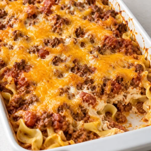 Ground Beef Casserole with egg noodles, tomato beef sauce, and melted Cheddar in a white baking dish