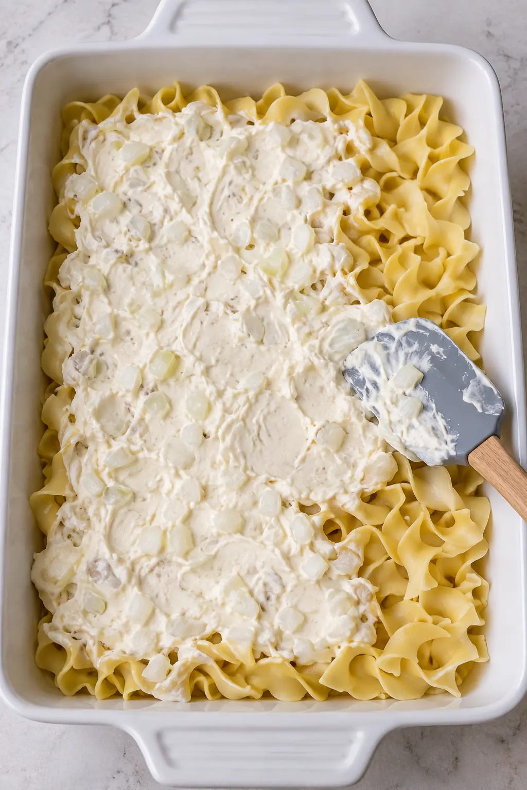 Creamy onion filling being spread over a layer of cooked egg noodles