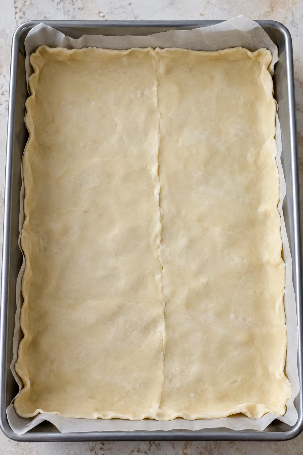 Unbaked pie crust fitted into a parchment-lined rectangular pan with the center seam pressed closed
