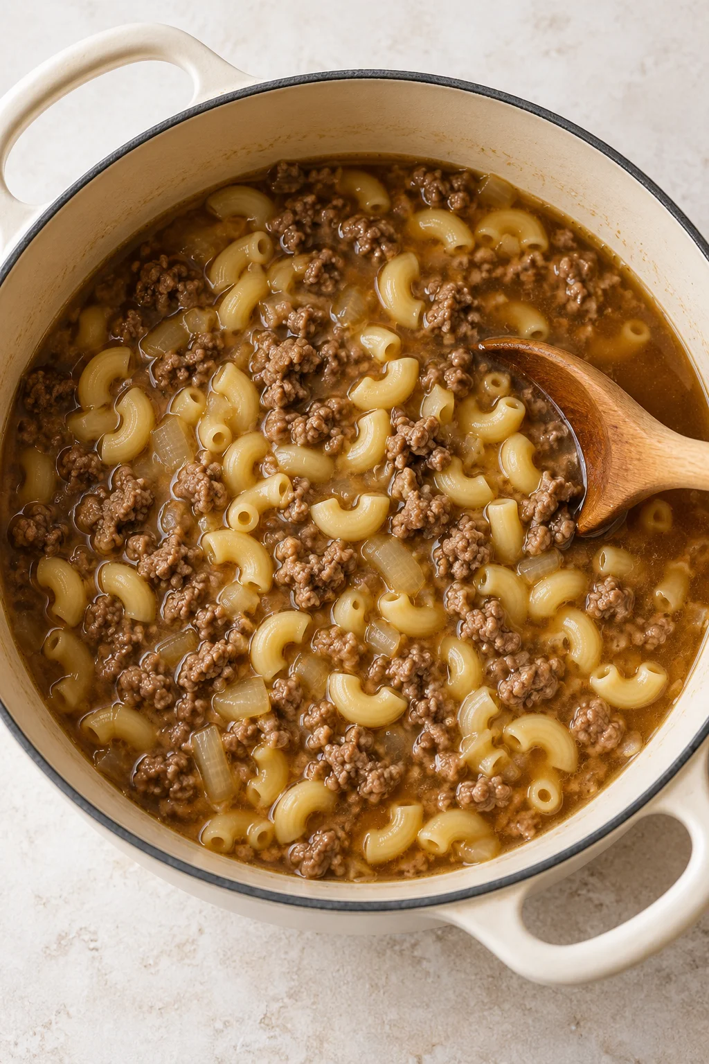 Elbow macaroni and browned ground beef simmering in beef broth before milk and cheese are added