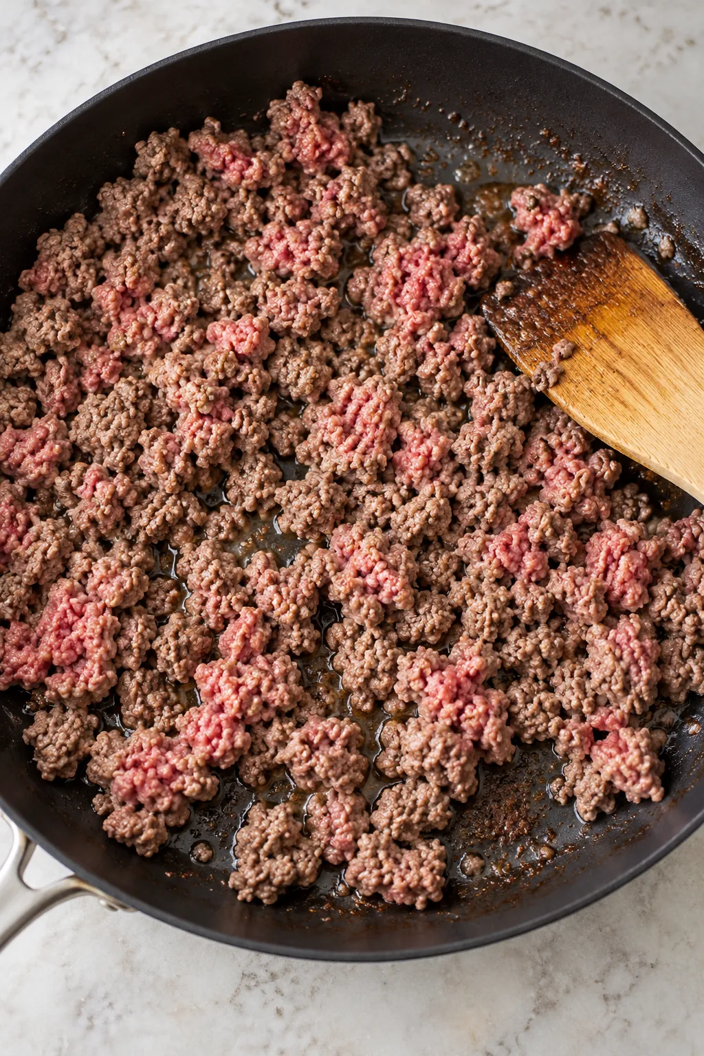 Ground beef partly browning in a skillet before the peppers and onion are added