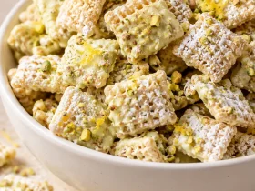 Finished pistachio lemon puppy chow with powdered sugar, chopped pistachios, and lemon zest in a white bowl