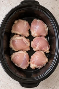 Six thawed chicken thighs arranged in one layer inside a black slow cooker