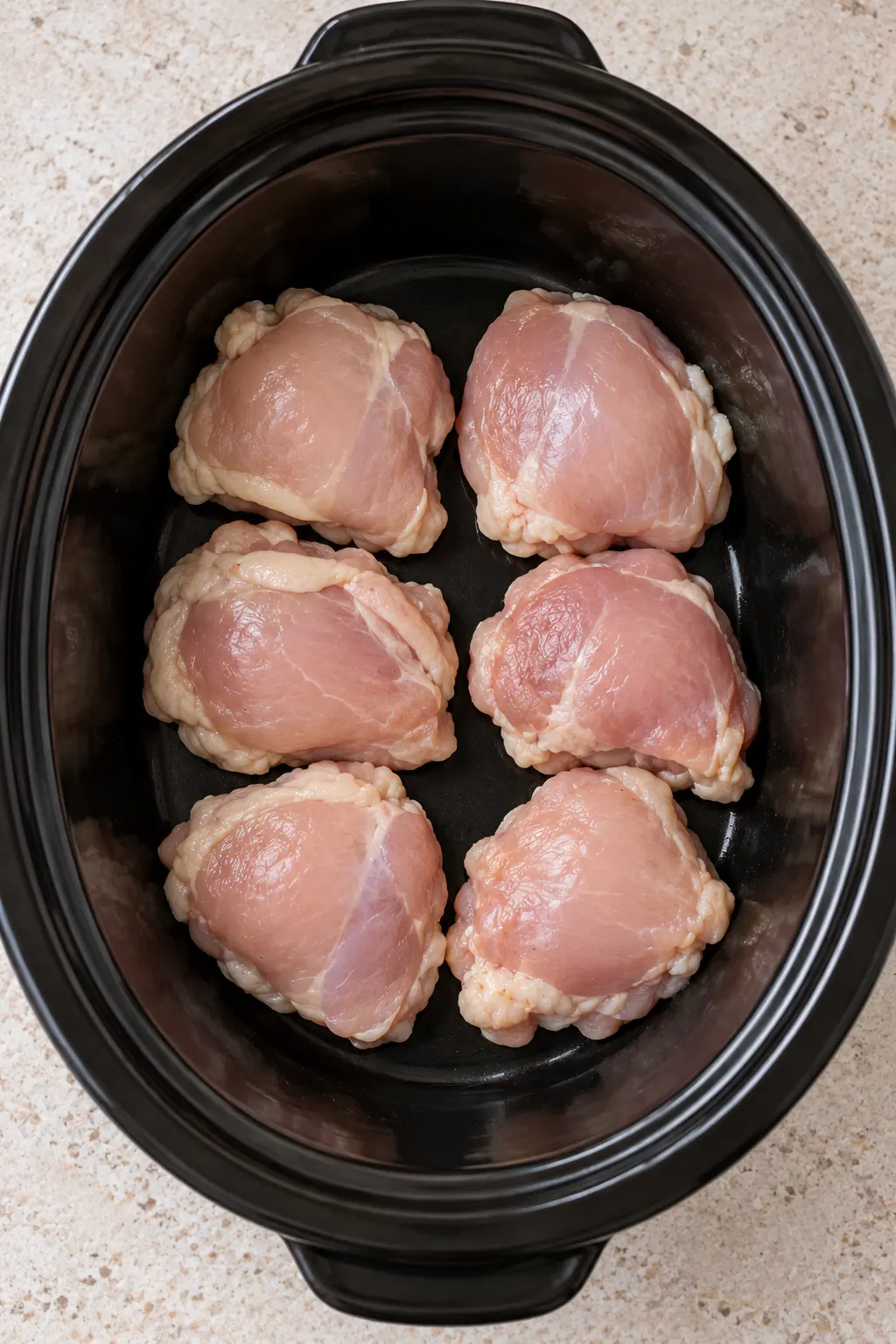 Six thawed chicken thighs arranged in one layer inside a black slow cooker