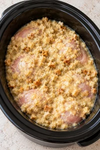 Creamy stuffing mixture spread over uncooked chicken thighs in a black slow cooker