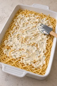 A thin seasoned cream cheese layer spread over the cooked spaghetti.