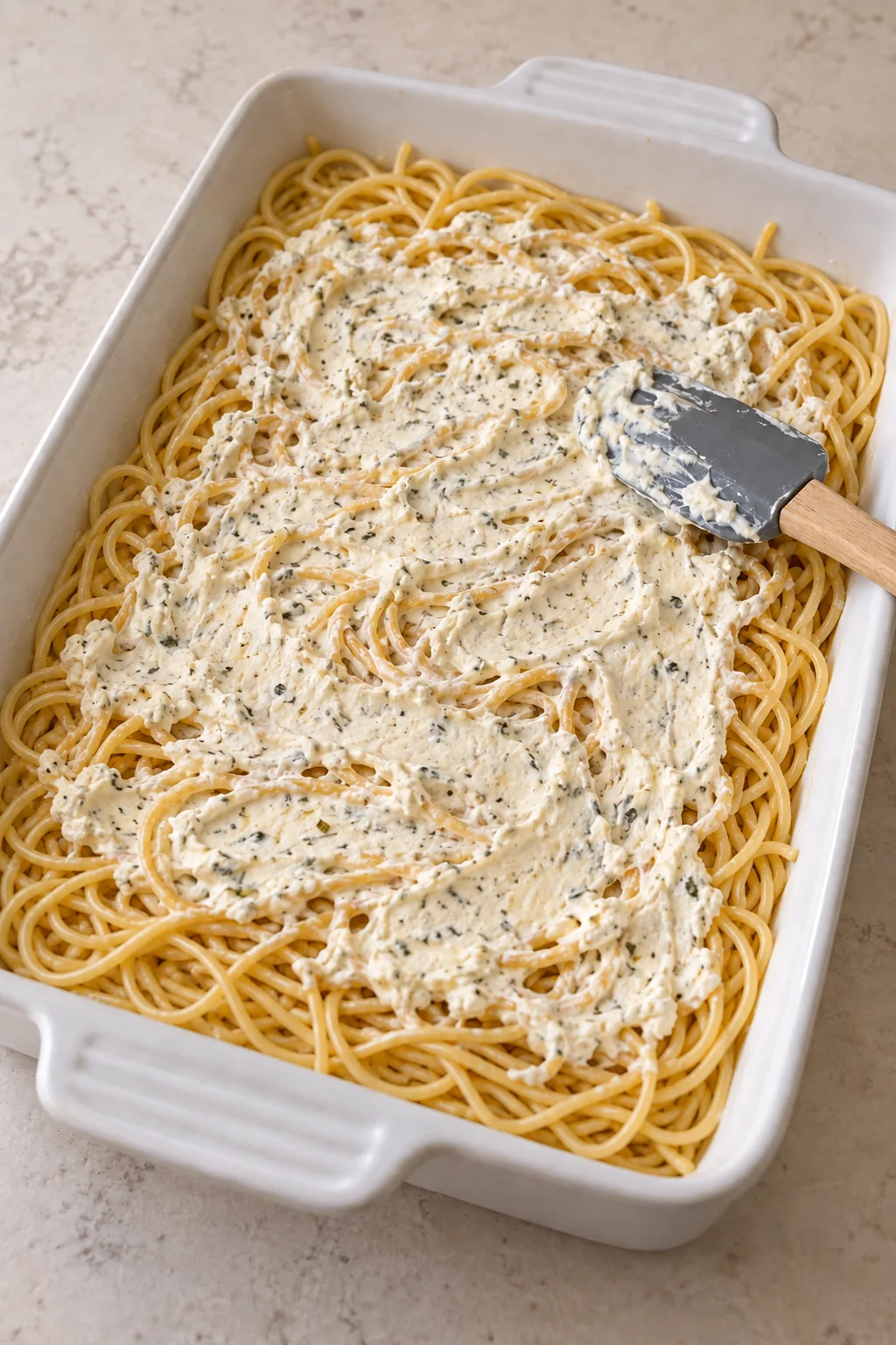 A thin seasoned cream cheese layer spread over the cooked spaghetti.