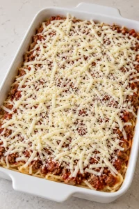 Unbaked spaghetti casserole topped with shredded mozzarella and grated Parmesan.