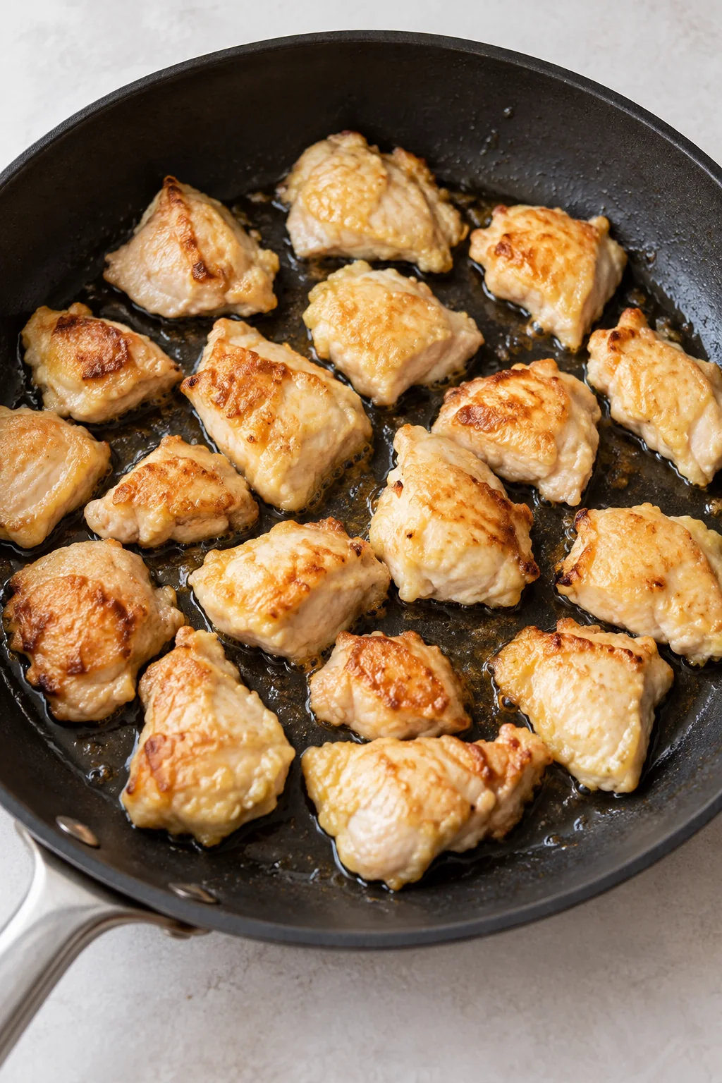 Chicken pieces with a light cornstarch and egg coating searing in a skillet.