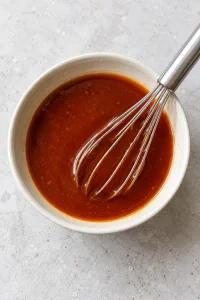 Whisked sweet and sour sauce in a small bowl with a whisk.