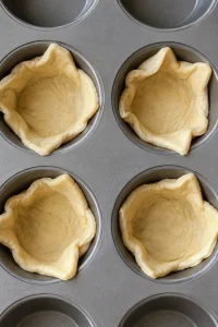 Unbaked crescent dough triangles pressed into standard muffin cups