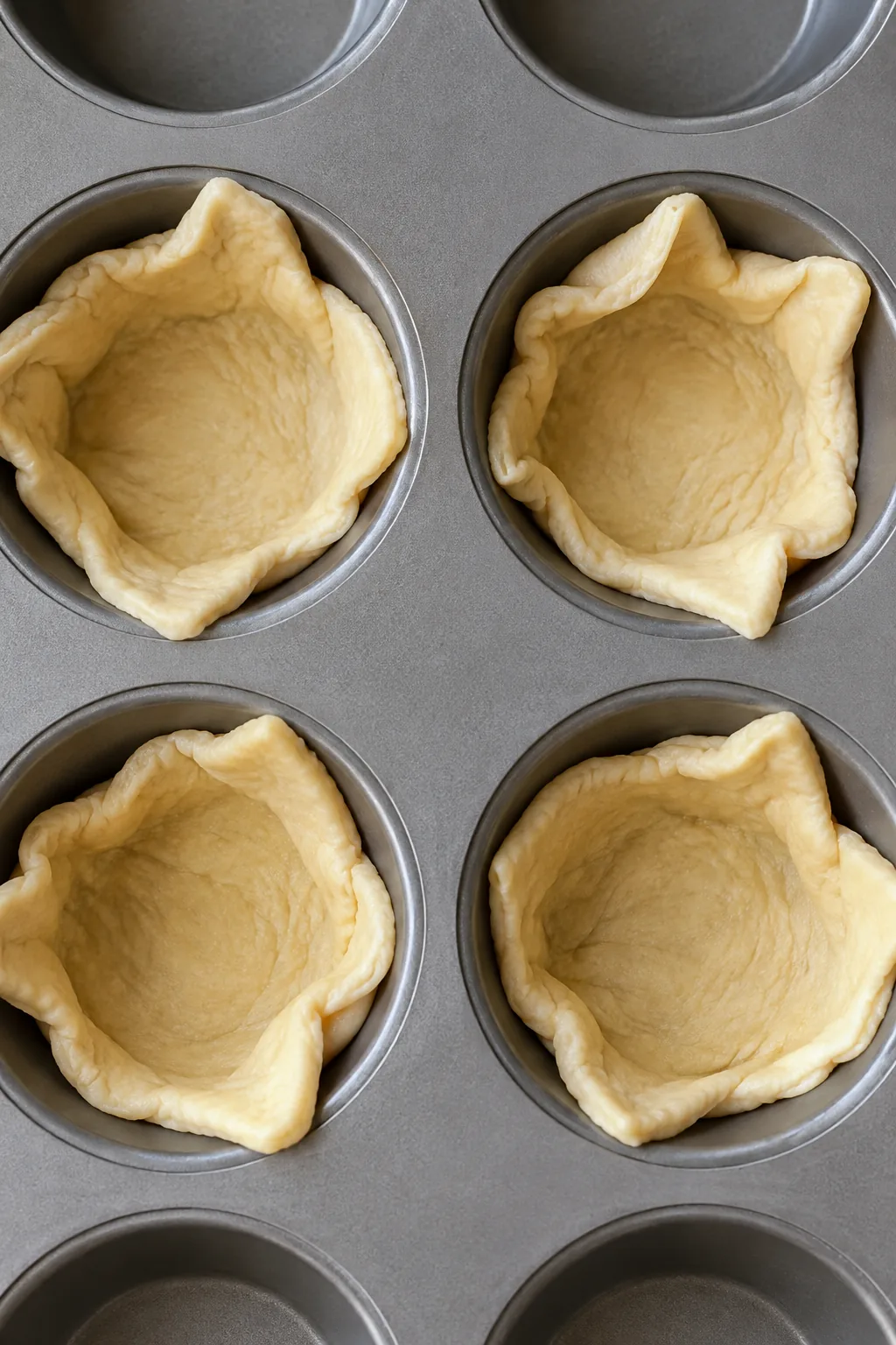 Unbaked crescent dough triangles pressed into standard muffin cups