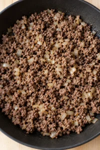Browned ground beef crumbles with finely diced onion in a skillet