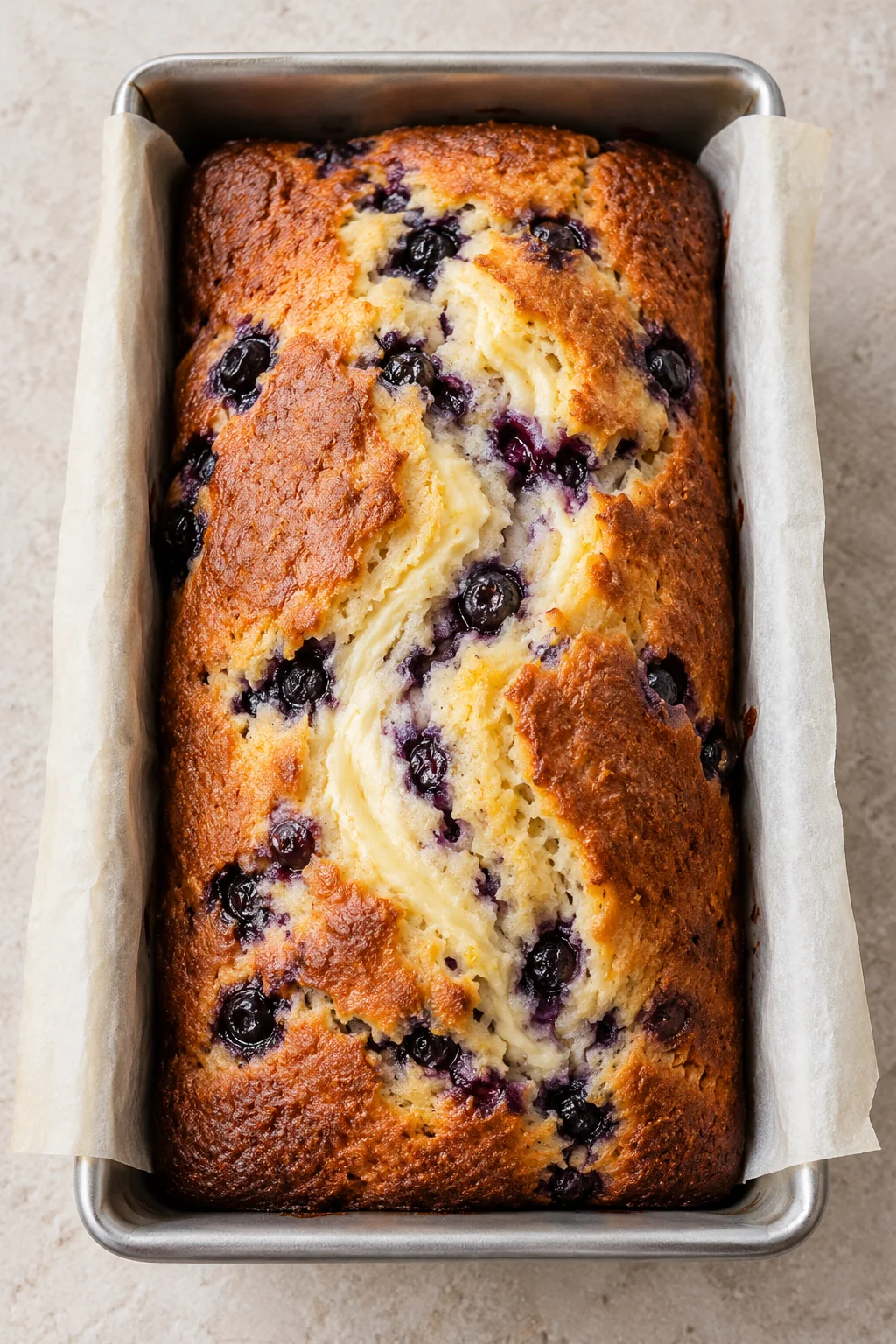 Golden blueberry cream cheese loaf cooling in its parchment-lined pan