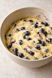 Fresh blueberries folded into thick lemon loaf batter in a mixing bowl