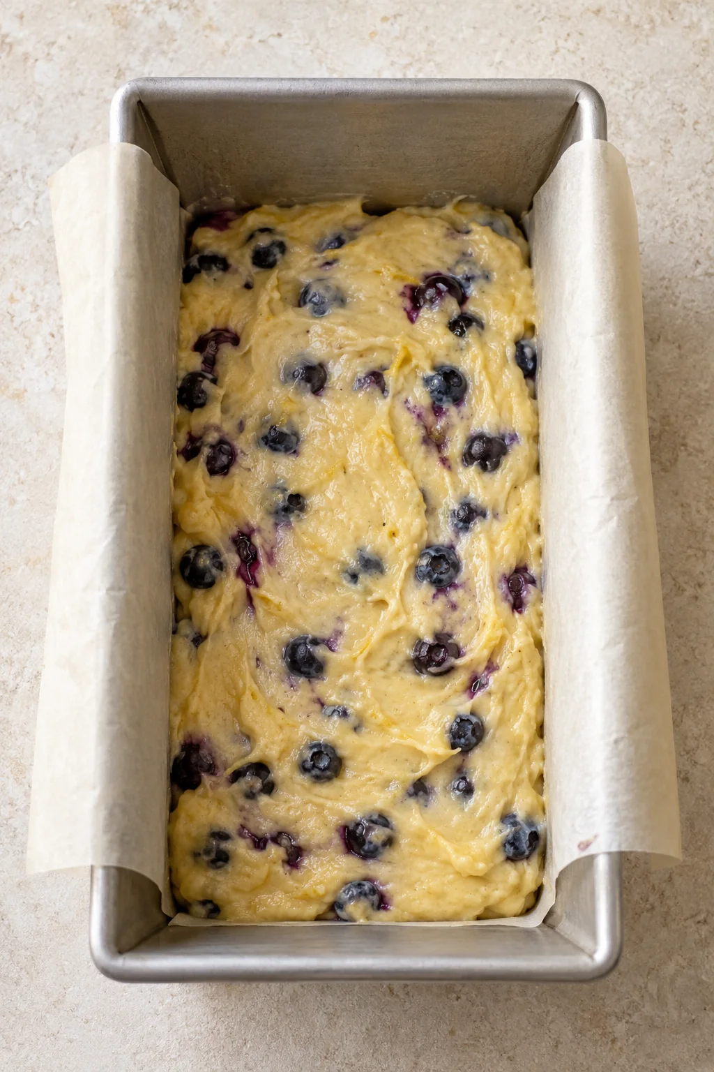 First layer of blueberry batter in a parchment-lined metal loaf pan