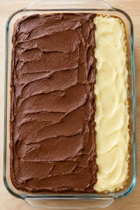 Chocolate frosting partly spread over the chilled vanilla pudding layer
