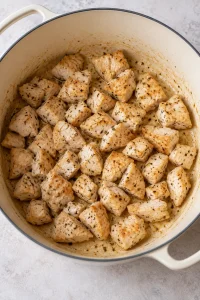 Bite-size chicken breast pieces lightly browned in butter in a large enamel pot