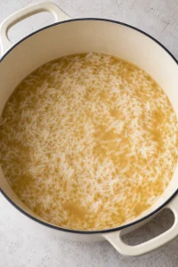 White long-grain rice simmering in chicken broth in a large enamel pot before broccoli is added