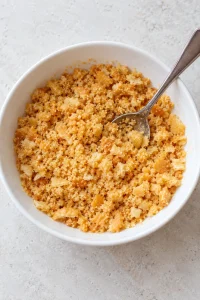 Crushed golden Ritz crackers mixed with melted butter in a small white bowl