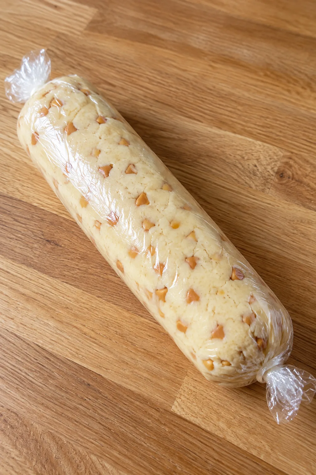 One wrapped shortbread dough log with butterscotch chips visible through the clear wrap