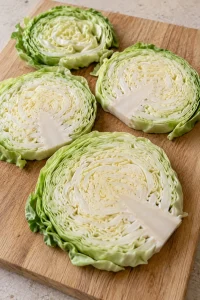 Thick raw green cabbage slices on a pale wooden board before seasoning