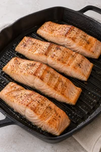 Salmon fillets cooking in a ridged grill pan before the honey butter finish