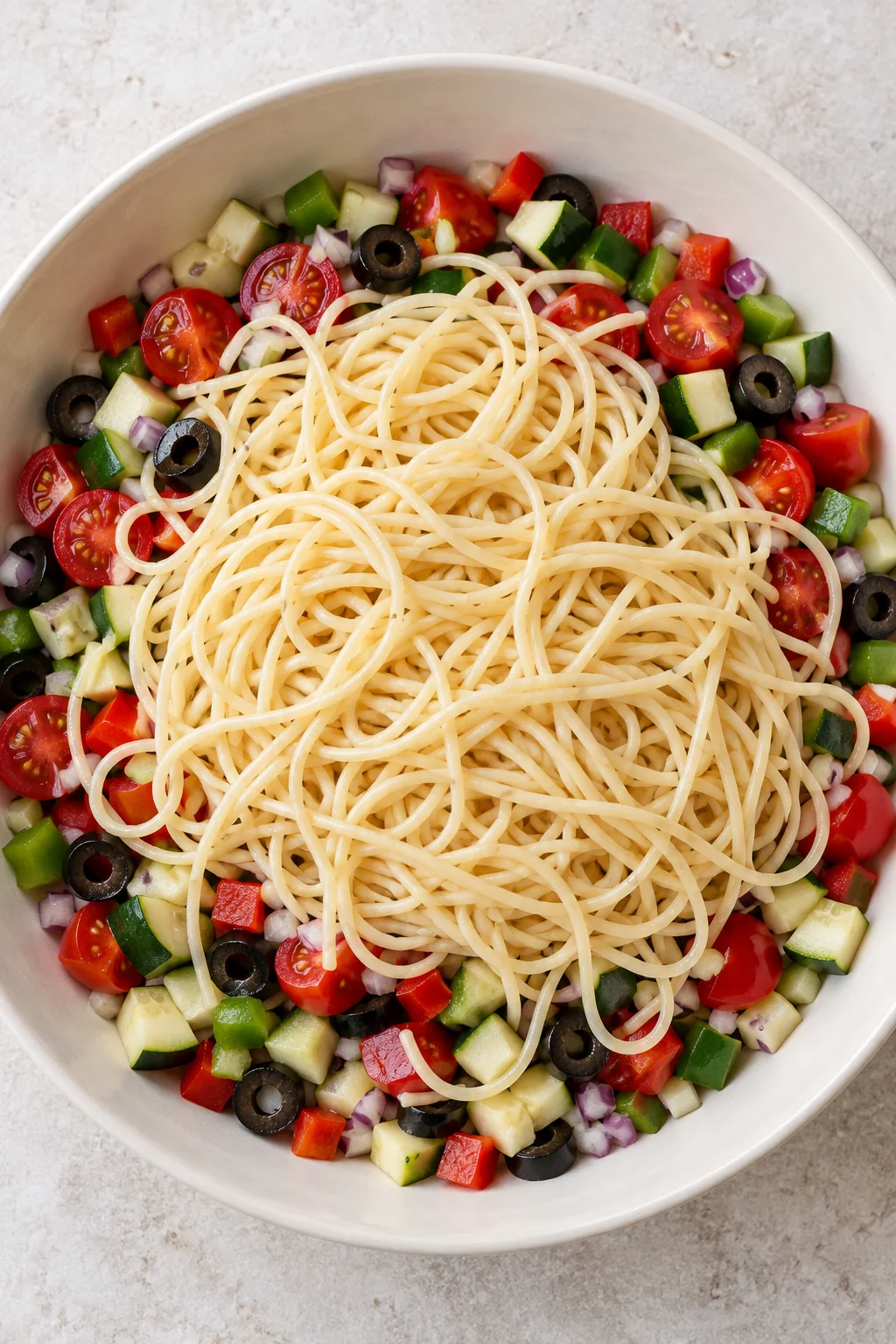 Cooled spaghetti added to the bowl of chopped vegetables before dressing