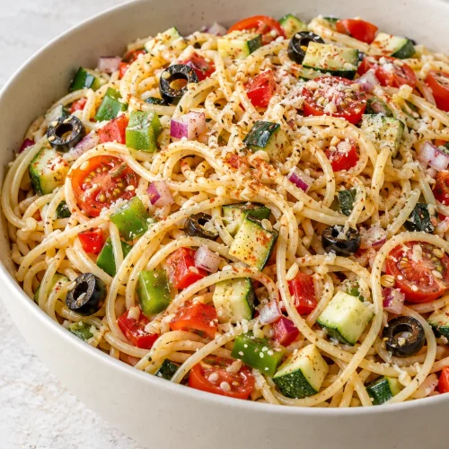 California spaghetti salad with colorful vegetables and sliced black olives in an ivory bowl