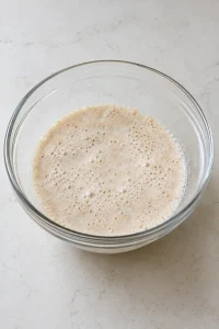 Foamy yeast on warm milk in a clear mixing bowl
