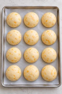 Twelve shaped cheddar buns puffed up after their second rise