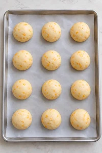 Twelve small cheddar dough balls shaped on a parchment-lined sheet pan