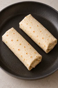 Two folded chicken wraps placed seam-side down in a nonstick skillet