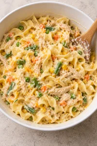 Wide cooked egg noodles folded into creamy chicken, cheese, and mixed vegetable filling in a mixing bowl
