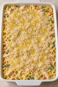 Unbaked chicken noodle casserole topped with pale Panko breadcrumbs and drizzled melted butter