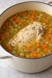 Bone-in chicken breast cooking in seasoned broth with carrots and celery.